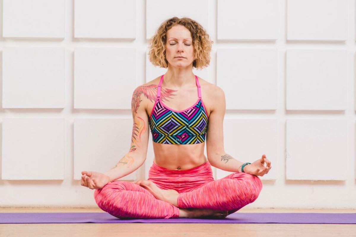 A person sitting cross-legged on a yoga mat, wearing a vibrant athletic outfit, practicing meditation with hands in a mudra gesture.