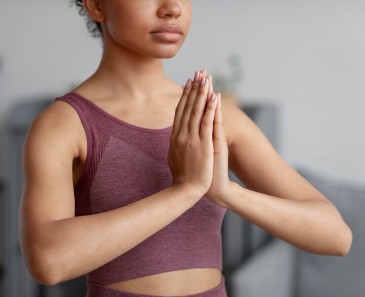 A person in a maroon athletic outfit practices yoga, with hands pressed together in a prayer position, set in a serene indoor space.
