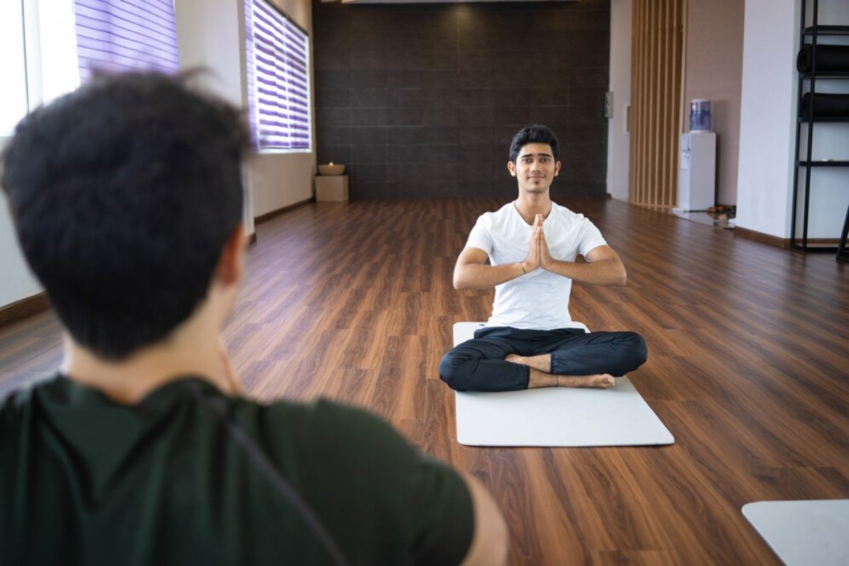 A peaceful yoga studio with two individuals practicing meditation on mats. Natural light filters through the window.