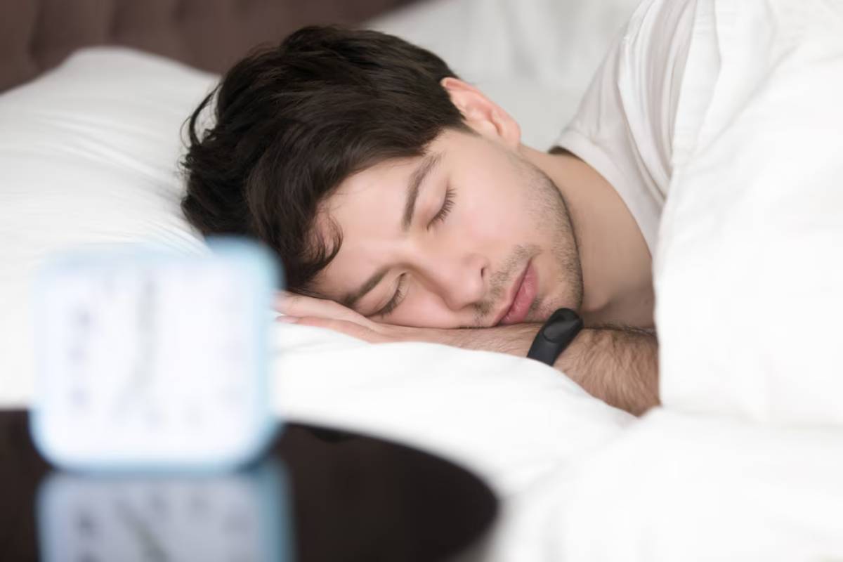 A person sleeps peacefully on a white bed, with a bedside clock in foreground, creating a serene morning atmosphere.