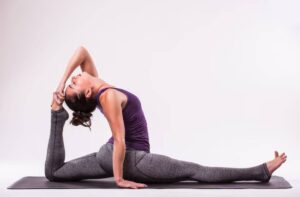 A person performs an advanced yoga pose, stretching in a deep backbend while sitting on a yoga mat.