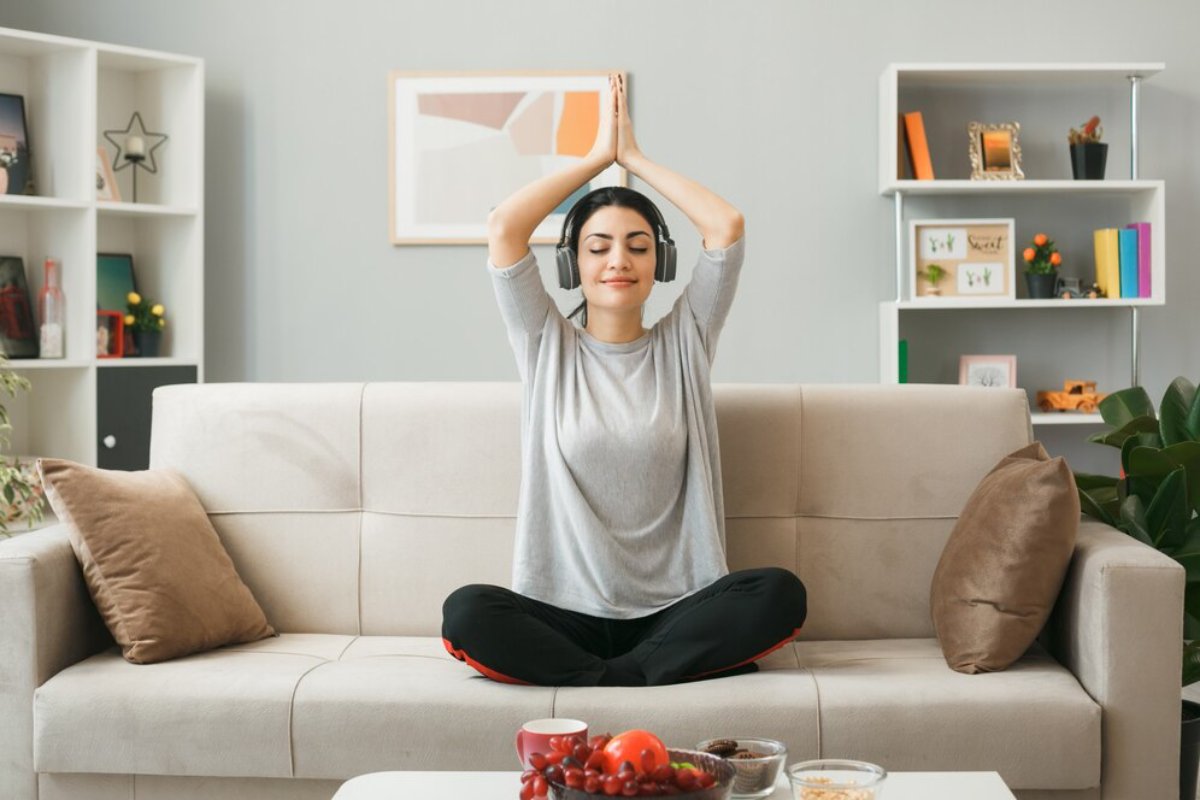 A person sitting cross-legged on a couch, wearing headphones, practicing meditation in a cozy, well-decorated living room.