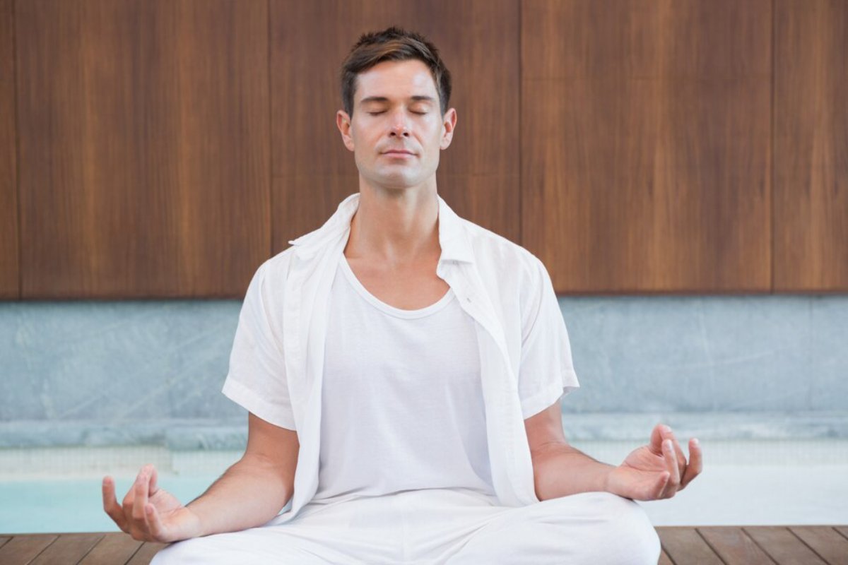 A person sits cross-legged in a serene space, wearing a white outfit, practicing meditation with hands in a relaxed position.