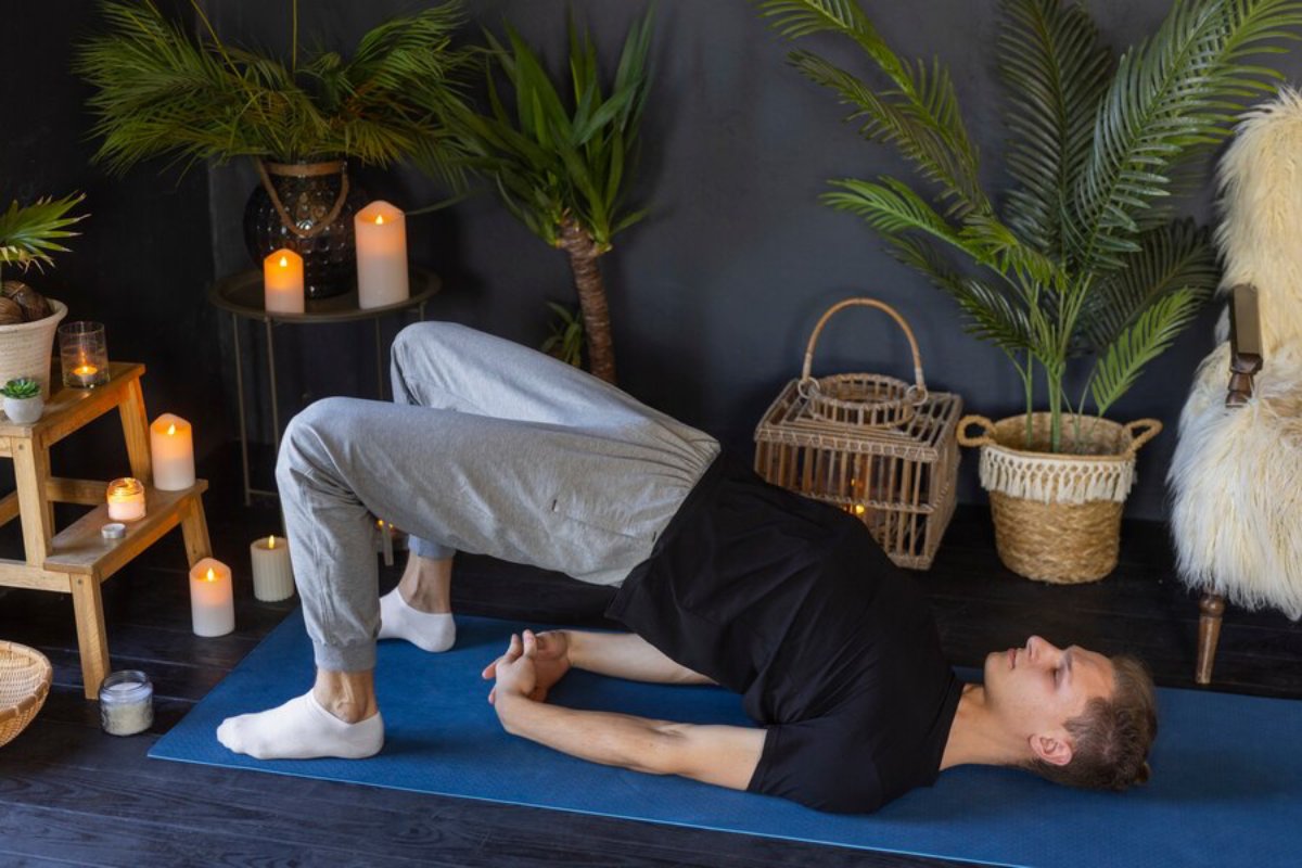 A person performs a bridge pose on a yoga mat surrounded by candles and lush plants in a calm, cozy indoor setting.