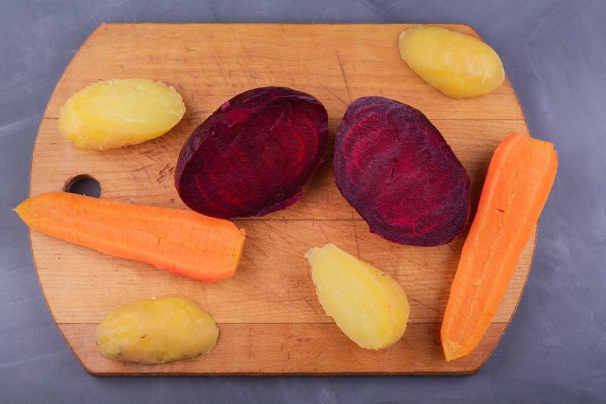 Variety of raw vegetables on a wooden cutting board: sliced beets, a carrot, and whole potatoes.