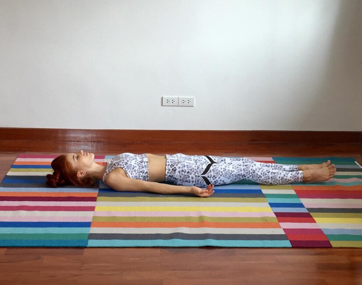 A person lies in a yoga pose on a colorful striped mat in a bright, minimalistic room, focusing on relaxation and mindfulness.