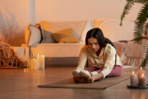 A person stretches on a yoga mat in a cozy living room with soft lighting, candles, and a couch with decorative pillows.