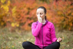 A person sits cross-legged outdoors, practicing mindfulness with a colorful autumn backdrop of orange and yellow foliage.