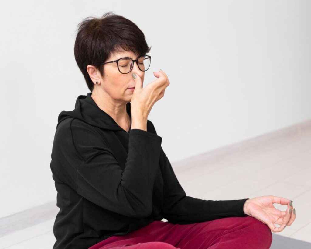 A person is practicing mindful breathing, seated in a meditative pose, wearing a black hoodie and burgundy pants in a calm, minimalist space.